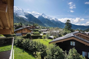 A mountain village with traditional wooden houses, lush greenery, and snow-capped peaks in the background.