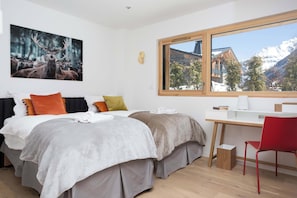 Une chambre d’hôtel avec deux lits, un bureau, une chaise, une fenêtre donnant sur la montagne et une œuvre d’art représentant des bois de cerf accrochée au mur.