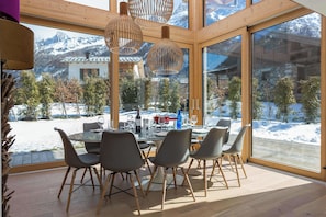 A modern dining area with a glass table and chairs, large windows, and a view of a snowy landscape. - Luxe Chalet Montana - Hot Tub - Chamonix All Year (Chamonix)