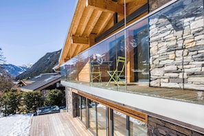 Un chalet moderne doté d’un balcon en verre offrant une vue imprenable sur un paysage montagneux enneigé.