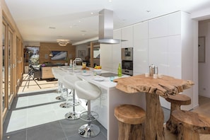 A modern kitchen with a central island, bar stools, and a wooden table with stools.