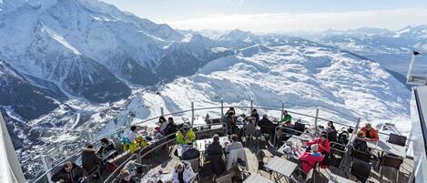 A high-altitude restaurant with outdoor seating overlooking a snowy mountain landscape.