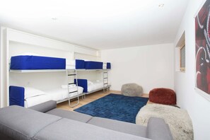 A dormitory room with bunk beds, a grey sofa, a blue rug, and a fluffy ottoman. - Luxe Chalet Montana - Hot Tub - Chamonix All Year (Chamonix)