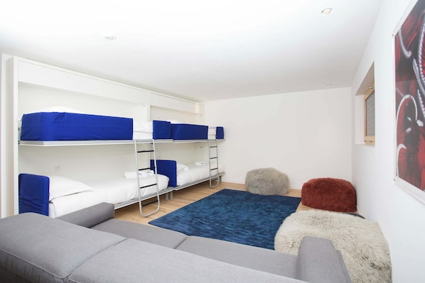 A dormitory room with bunk beds, a grey sofa, a blue rug, and a fluffy ottoman.