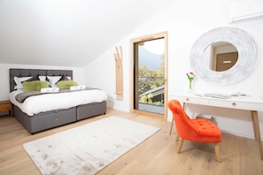 Un dormitorio con cama, escritorio, silla, espejo y vistas al exterior.