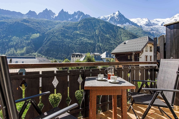 A balcony with a table and chairs, overlooking a mountainous landscape with snow-capped peaks.