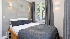 Un dormitorio con cama, ventana con cortinas e iluminación en la pared.