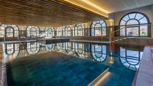 A spacious indoor swimming pool with a clear view of the outdoors through large arched windows.
