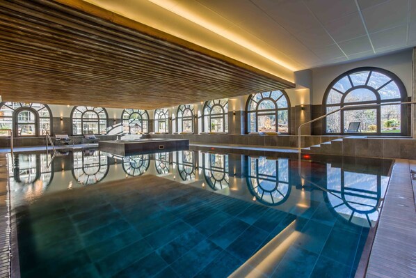 A large indoor swimming pool with arched windows and a wooden ceiling.