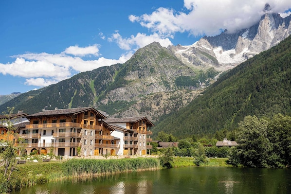 A mountain lodge with multiple wooden buildings, a lake, and a backdrop of snow-capped peaks.
