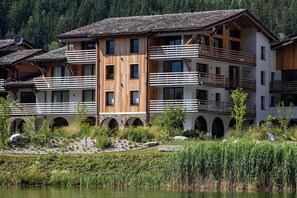 A multi-story building with balconies, arched windows, and a surrounding garden with a pond.