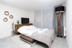 Une chambre à coucher moderne avec un lit, un téléviseur, une armoire en bois et une grande lampe sur pied.