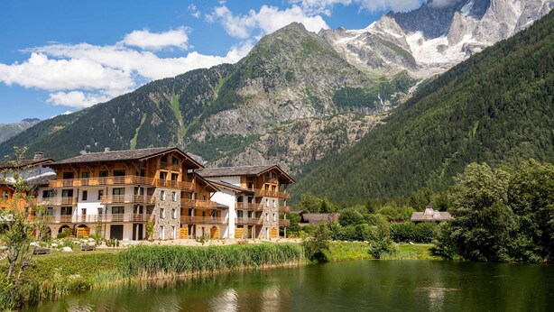 A mountain lodge with multiple floors, wooden balconies, and a view of a lake and mountains.