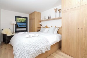 A bedroom with a bed, a TV, wooden wardrobe, and a window with a view of a forest. - La Cordee 412 Apt - Lakefront - Chamonix All Year (Les Praz,)
