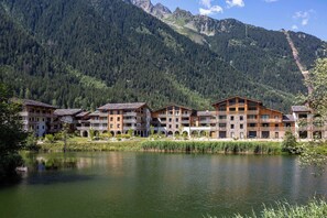 A hotel with multiple buildings, a lake in front, and mountains in the background. - La Cordee 412 Apt - Lakefront - Chamonix All Year (Les Praz,)