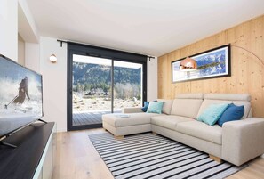 Een moderne woonkamer met een groot raam, een hoekbank, een flatscreen televisie en een ingelijst kunstwerk aan de muur.