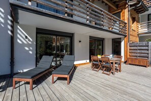 Une terrasse avec une table et des chaises, un fauteuil de relaxation et une rambarde en bois.