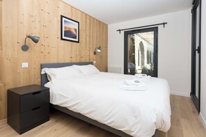 A bedroom with a bed, bedside tables, a wall-mounted picture, and a window with a view of an outdoor area.
