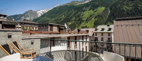 Una terraza con mesa y sillas de vidrio, con vistas a un paisaje montañoso y edificios al fondo.