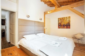 A bedroom with a bed, a headboard, a door, a wall-mounted artwork, and a chair.