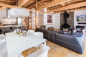 A modern living space with a dining area, a black leather sofa, a fireplace, and a kitchen with a white countertop.