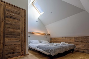 Een slaapkamer met een schuine kap, dakraam, een bed met witte lakens en houten wandbekleding.