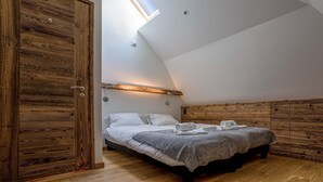 Una camera da letto con soffitto spiovente, un lucernario, un letto con coperta grigia e pannelli di legno sulle pareti.