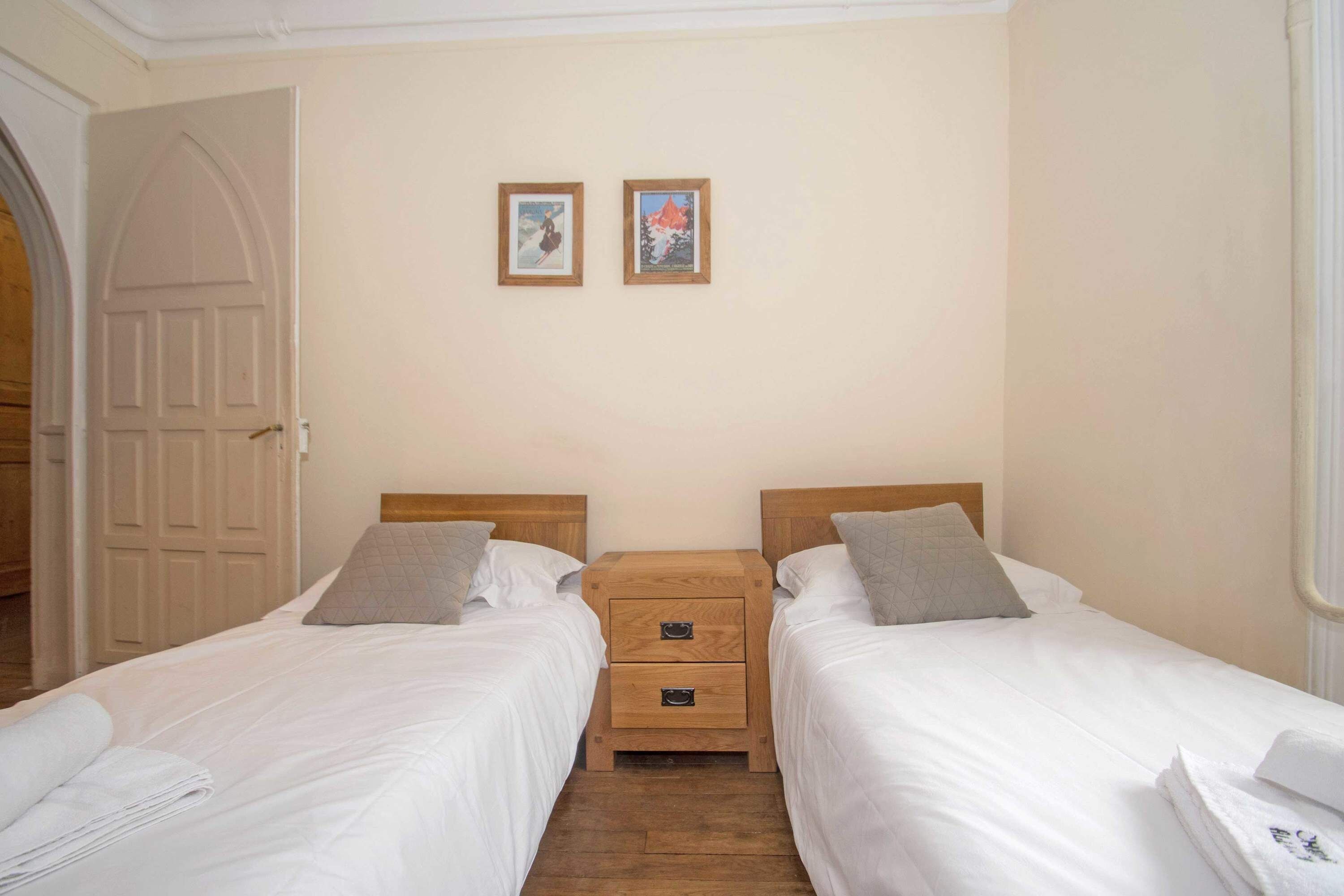 Een hotelkamer met twee eenpersoonsbedden, een houten nachtkastje en een deur.