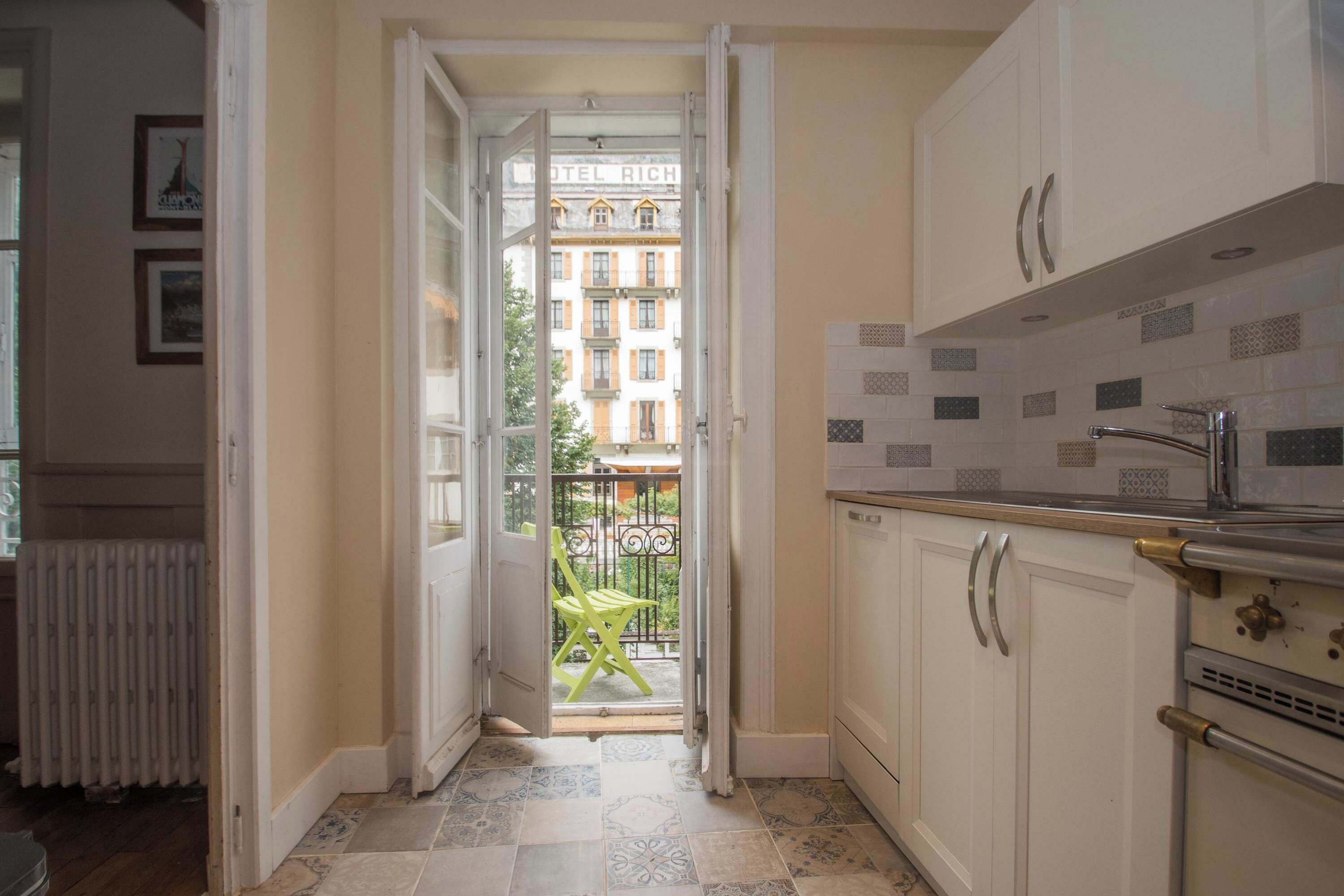 A narrow kitchen with white cabinets, a tiled backsplash, and a view of a building labeled 'HOTEL RICHARD' through an open door.