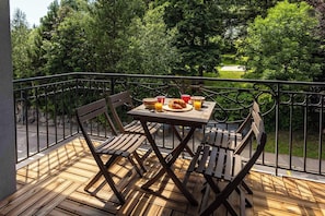 A wooden deck with a table and chairs, a croissant, and a glass of orange juice.