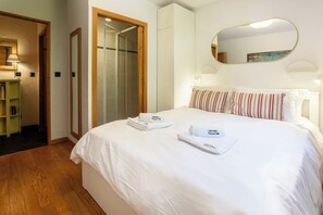 Une chambre d’hôtel avec un grand lit, une douche en verre, une porte en bois, une bibliothèque et un miroir au mur.