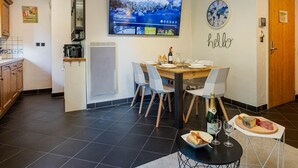 Eine moderne Küche mit Fernseher, einer Essecke mit Holztisch und Stühlen, einem kleinen runden Tisch mit Flasche und Gläsern sowie einem Schild an der Wand mit der Aufschrift 'hello'.