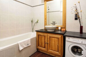 A bathroom with a bathtub, a sink with a mirror, wooden cabinets, and a washing machine.