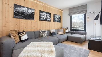 Un salon moderne avec un canapé d’angle, un plaid en fausse fourrure et trois photographies encadrées accrochées au mur.