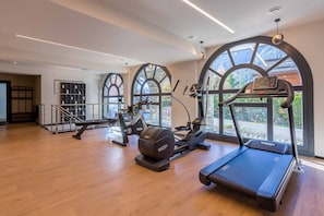 A gym with exercise equipment, large windows, and a wooden floor.