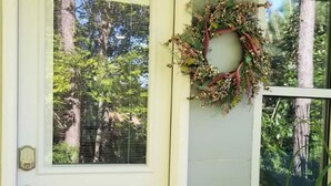 A white door with a glass panel, a wreath on the wall, and a window with a view of trees. - Cozy N. Raleigh Apt. with Pool and Hot Tub. Pets welcome BBQ Grill, TV & movies (Raleigh)