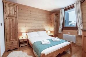 Ein Schlafzimmer mit Holzboden, einem Bett, Nachttischen, einem Kleiderschrank und einem Fenster mit Vorhängen.
