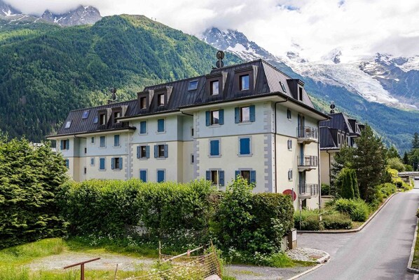 A multi-story hotel with a balcony, set against a mountainous backdrop.