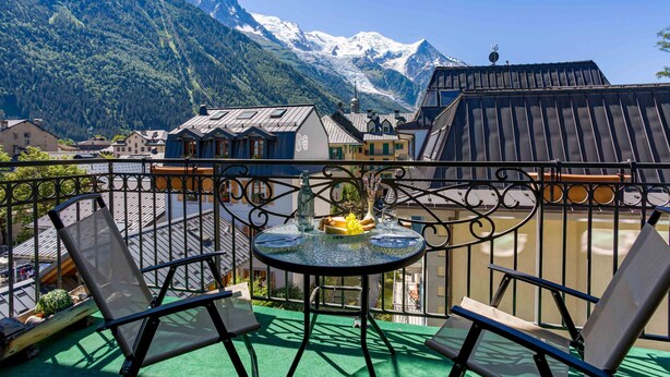 A balcony with two chairs and a table, overlooking a mountain and a town.