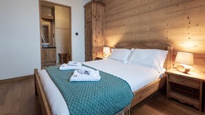 A bedroom with a wooden headboard, a bed with white linens, two bedside lamps, a wooden nightstand, and a bathroom visible through an open door.