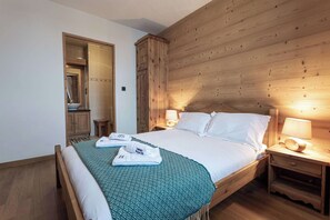Een hotelkamer met een houten hoofdbord, een bed met witte lakens, twee bedlampen en een klein houten nachtkastje.