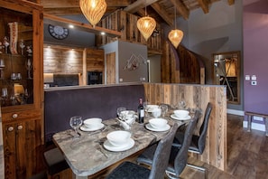 A dining area with a wooden table set for six, surrounded by chairs, and a wooden cabinet with glass doors on the left.