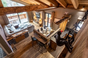 A spacious living area with a sofa, dining table, and chairs, a kitchen with a hanging light fixture, and a staircase with a decorative metal sculpture.