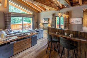 Une cuisine moderne avec un îlot central en bois, des tabourets de bar et un coin repas offrant une vue sur l’extérieur.