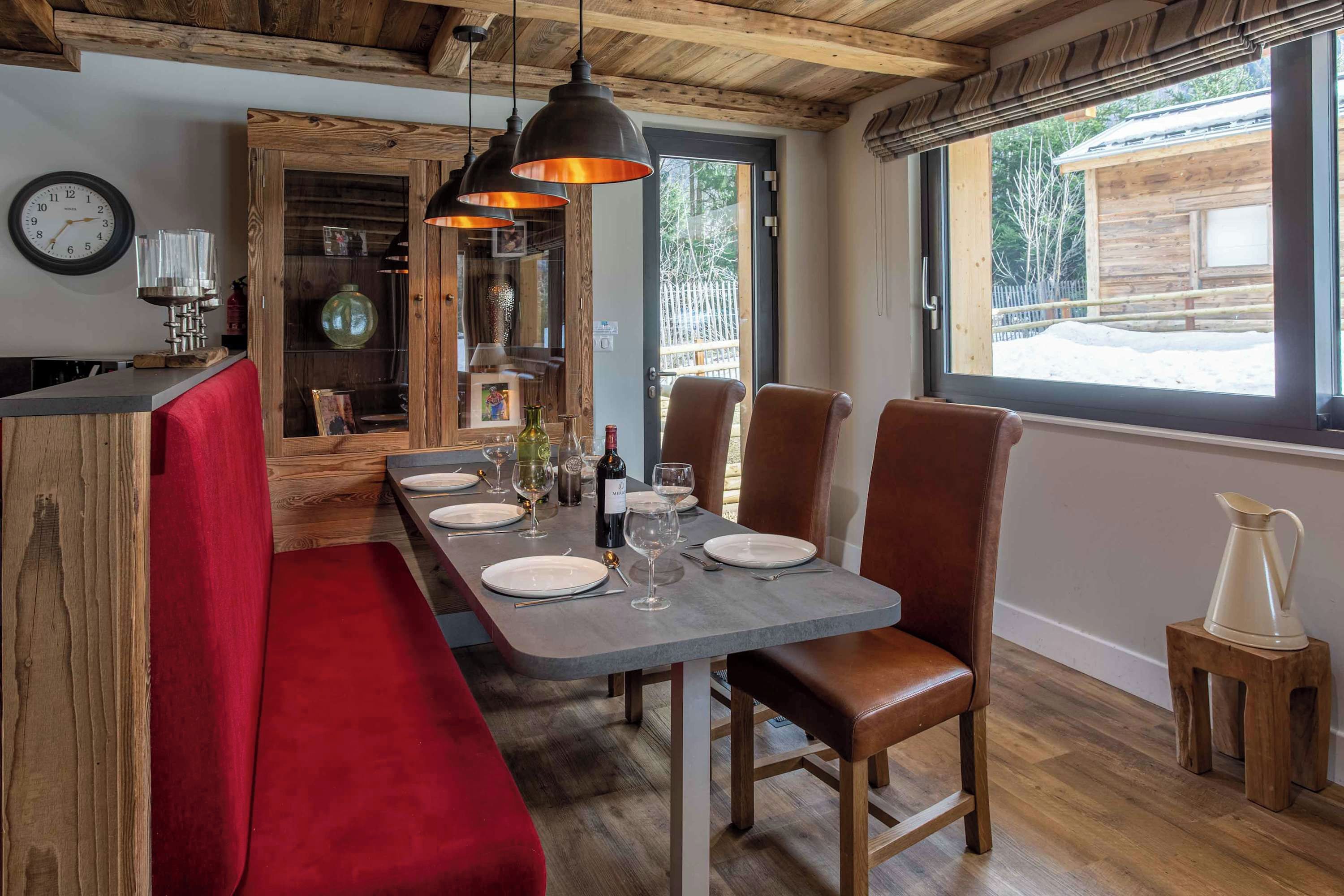 Un coin repas avec une table en bois dressée pour deux personnes, un banc et une vue sur l’extérieur.