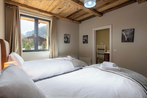 Habitación de hotel con dos camas, una ventana con cortinas, vigas de madera en el techo y vistas a la montaña.