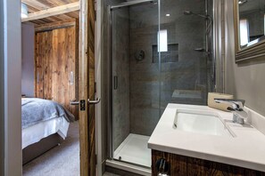 Een moderne badkamer met een douchecabine van glas, een witte wastafel en een houten deur naar een slaapkamer.