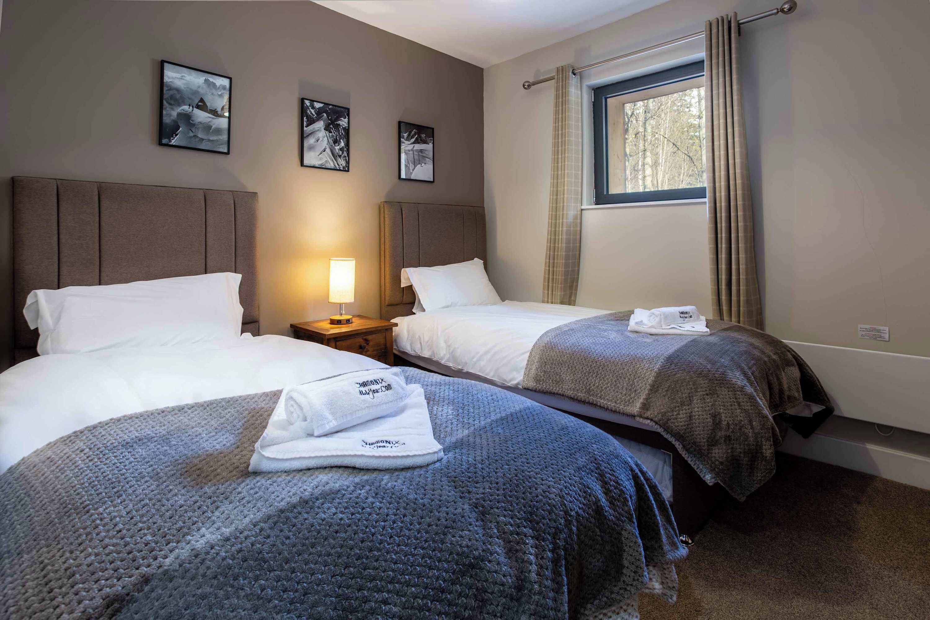 Habitación de hotel con dos camas, una mesita de noche, una lámpara y una ventana con cortinas.
