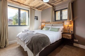Ein Schlafzimmer mit einem großen Bett, einem Holzkopfende, zwei Nachttischen, einer Nachttischlampe und einem Fenster mit Vorhängen.