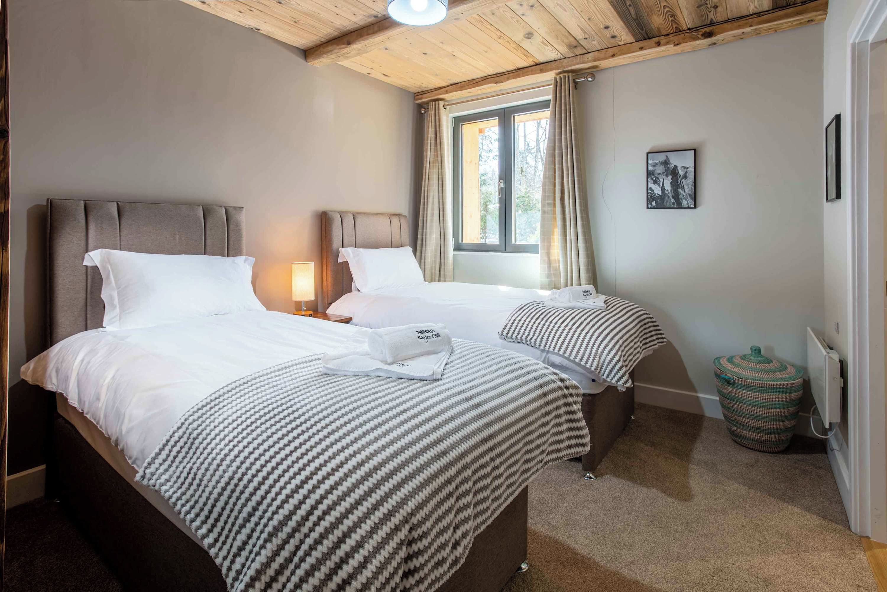 Ein Hotelzimmer mit zwei Betten, einem Vorhangfenster, einer Lampe, einem gerahmten Bild an der Wand und einer Heizung.
